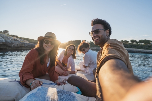 Group of friends smiling and relaxing on a boat at sunset, enjoying summer holiday moments